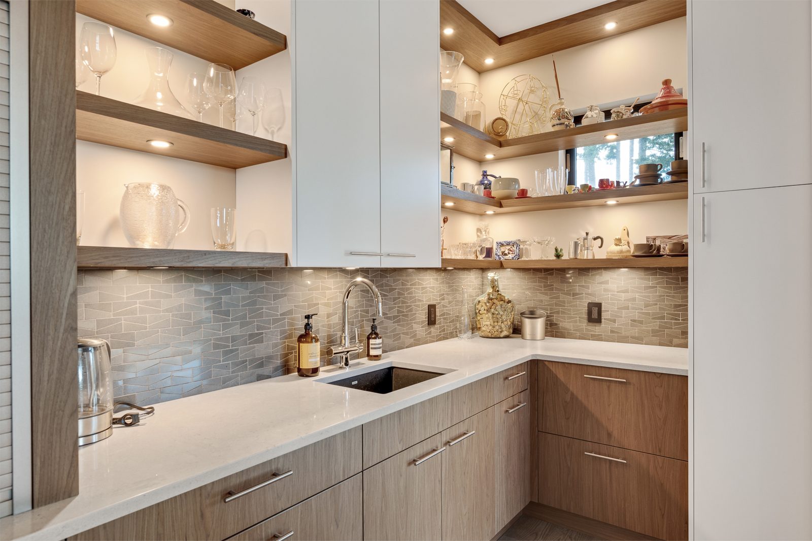 Butler pantry with lit open shelving, a second sink and glassware on floating oak shelves