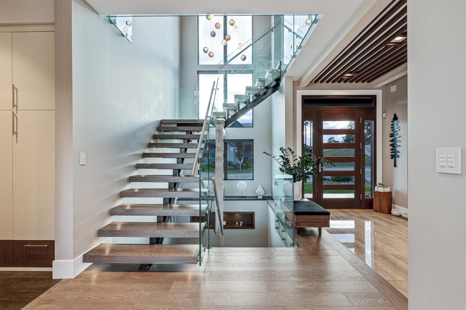 Open-riser oak stair with a steel spine and glass balustrade rising past a two-storey window wall