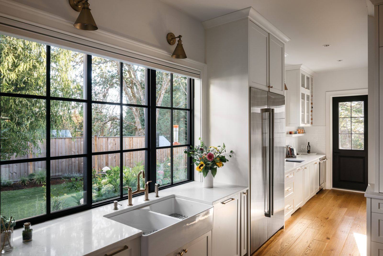 Kitchen sink run under a wall of black-framed windows looking out to a hydrangea border and lawn
