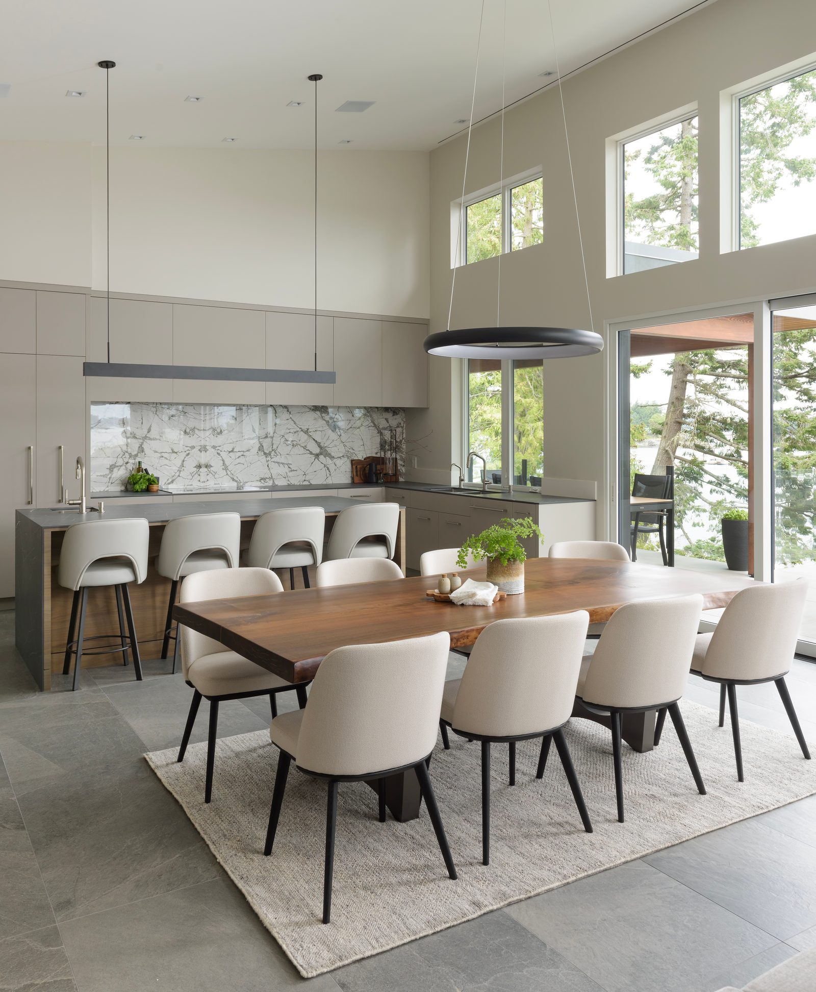 Dining table in live-edge walnut beside a grey kitchen with a book-matched marble backsplash