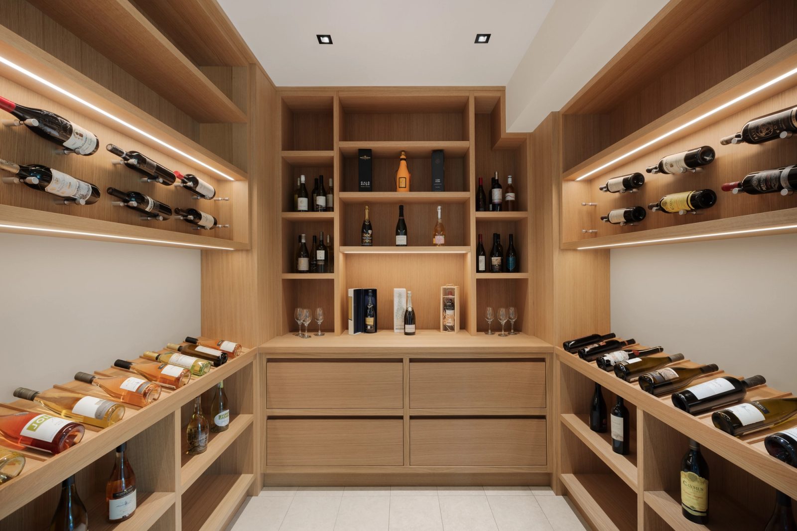 A wine room lined in pale oak, angled racks and lit shelving to three walls.