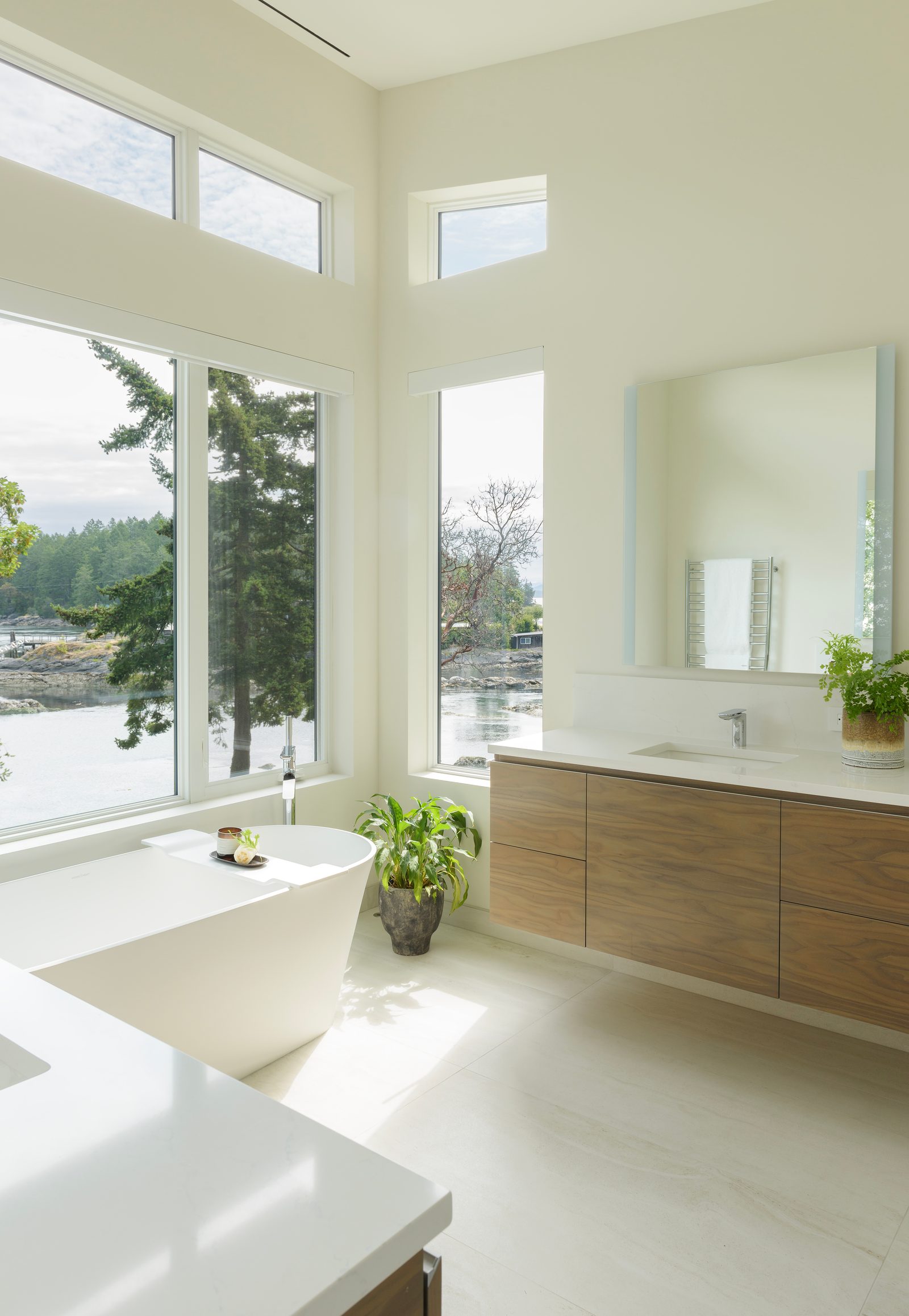 Ensuite with a freestanding tub set into a corner of glazing looking out to the shore and a walnut vanity