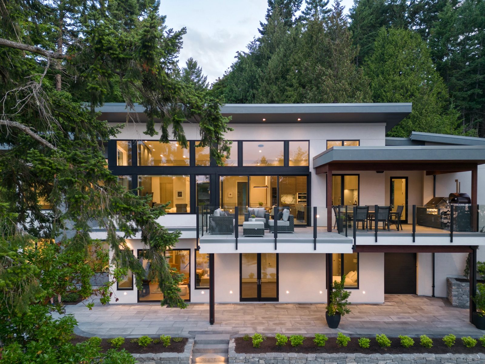 Waterfront elevation at dusk seen from the air, with two levels of deck and a fully glazed living wall lit from within