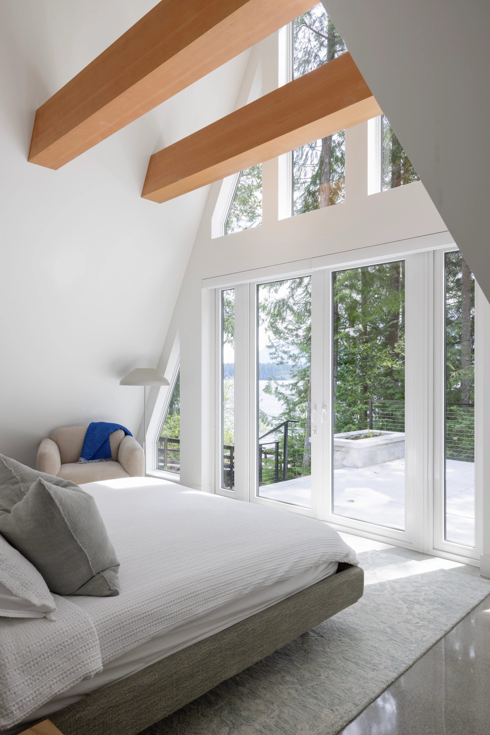 Bedroom under exposed fir beams with the lake through a glazed gable