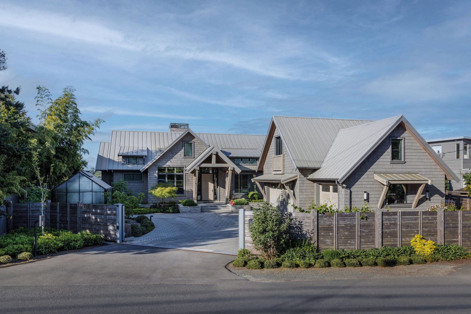 The house from the road, shingled gables and metal roof behind a gated paved drive
