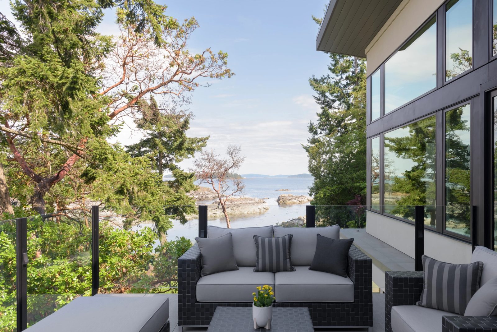 Covered deck with seating framed by an arbutus, looking across the channel to rocks and distant islands