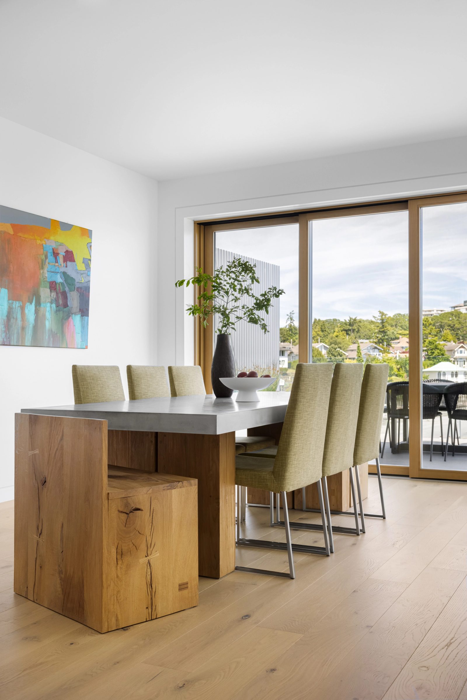 Concrete-topped dining table on solid timber blocks, upholstered chairs along one side and glass doors to a terrace.