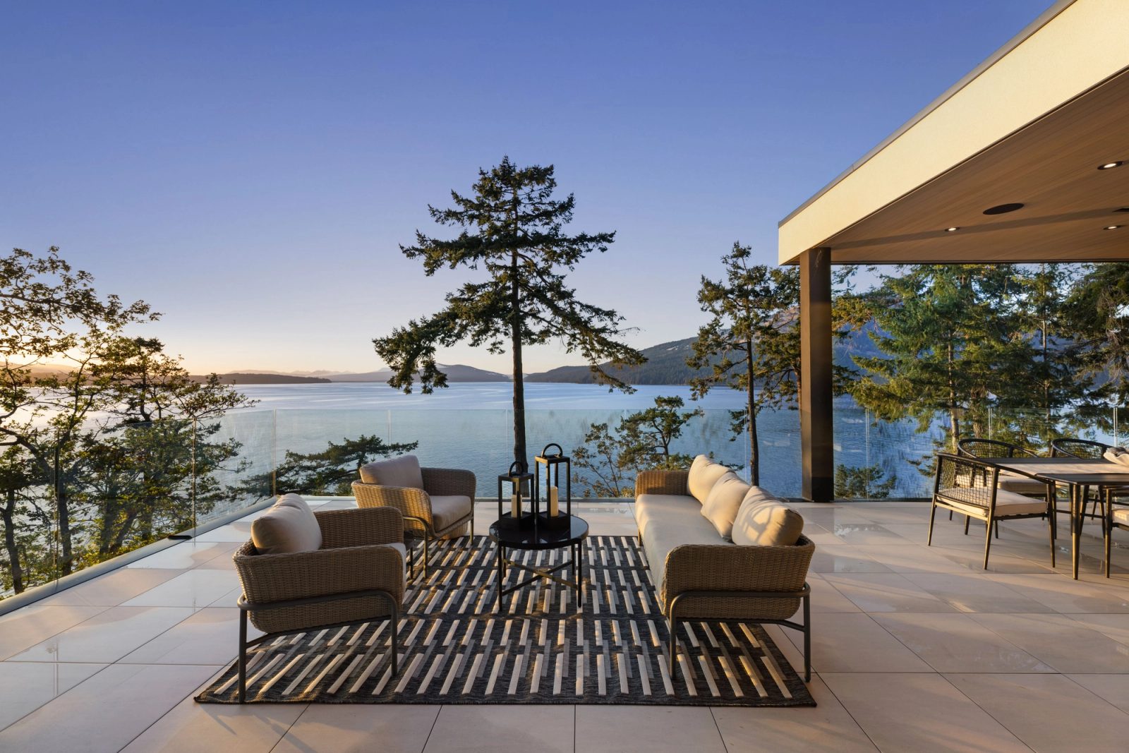 The view out from beneath a deep overhang: standing firs, the channel, and a forested island ridge across it, with no part of the house in frame.