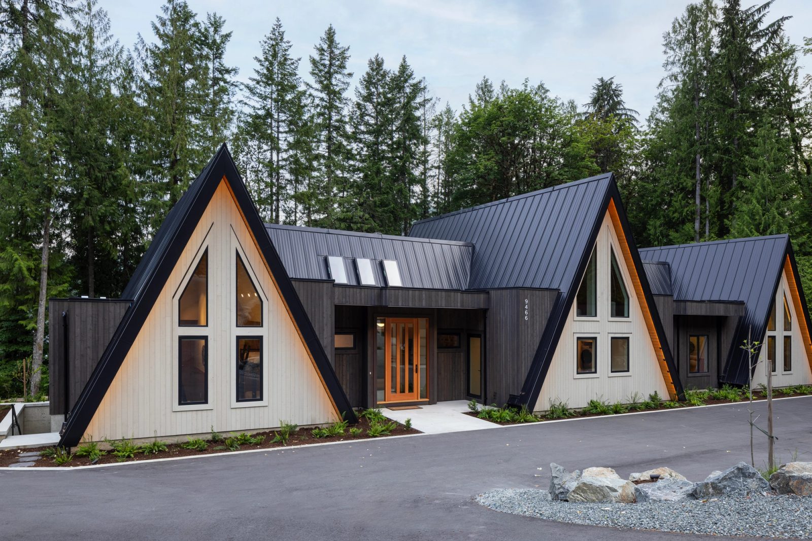Front elevation of three pale A-frame gables joined by flat-roofed links, fir entry door at centre