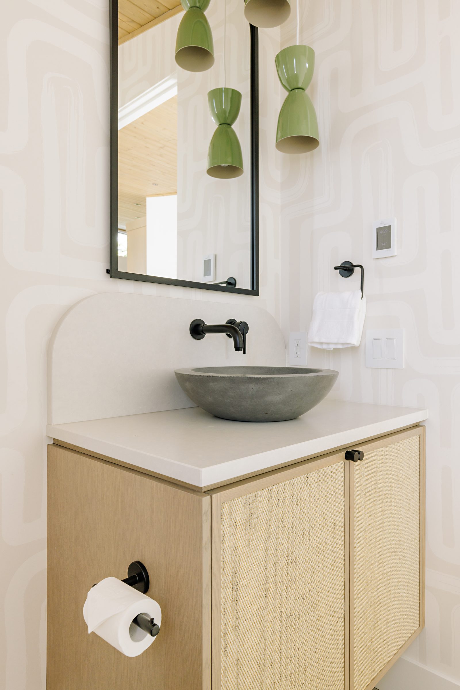 the same basin seen wider, with a cluster of green ceramic double-cone pendants hanging beside the mirror and a cane-fronted cabinet below.
