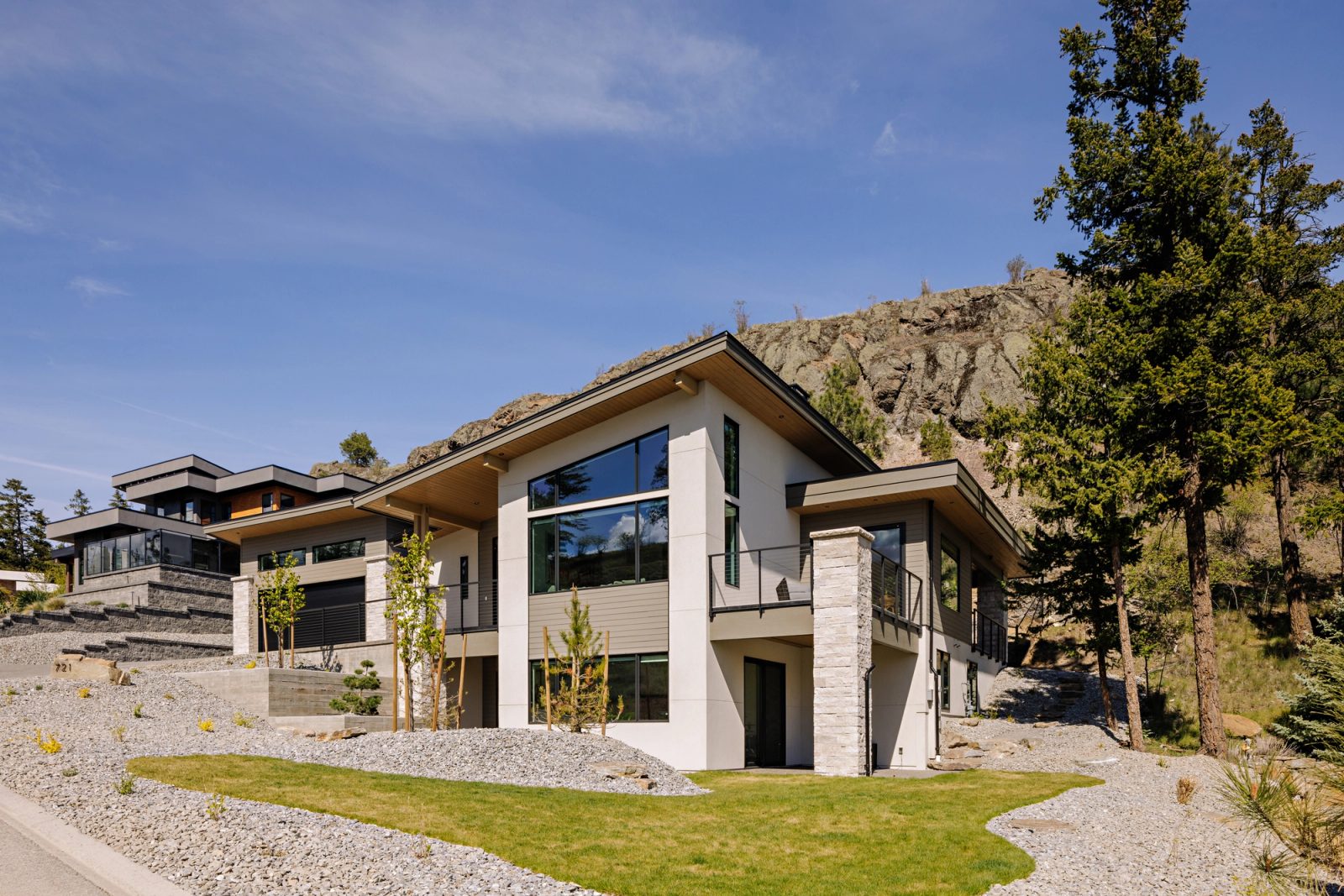 The same house seen at three-quarters from the road below, its low shed roofs stepping down the slope toward a gravel forecourt.