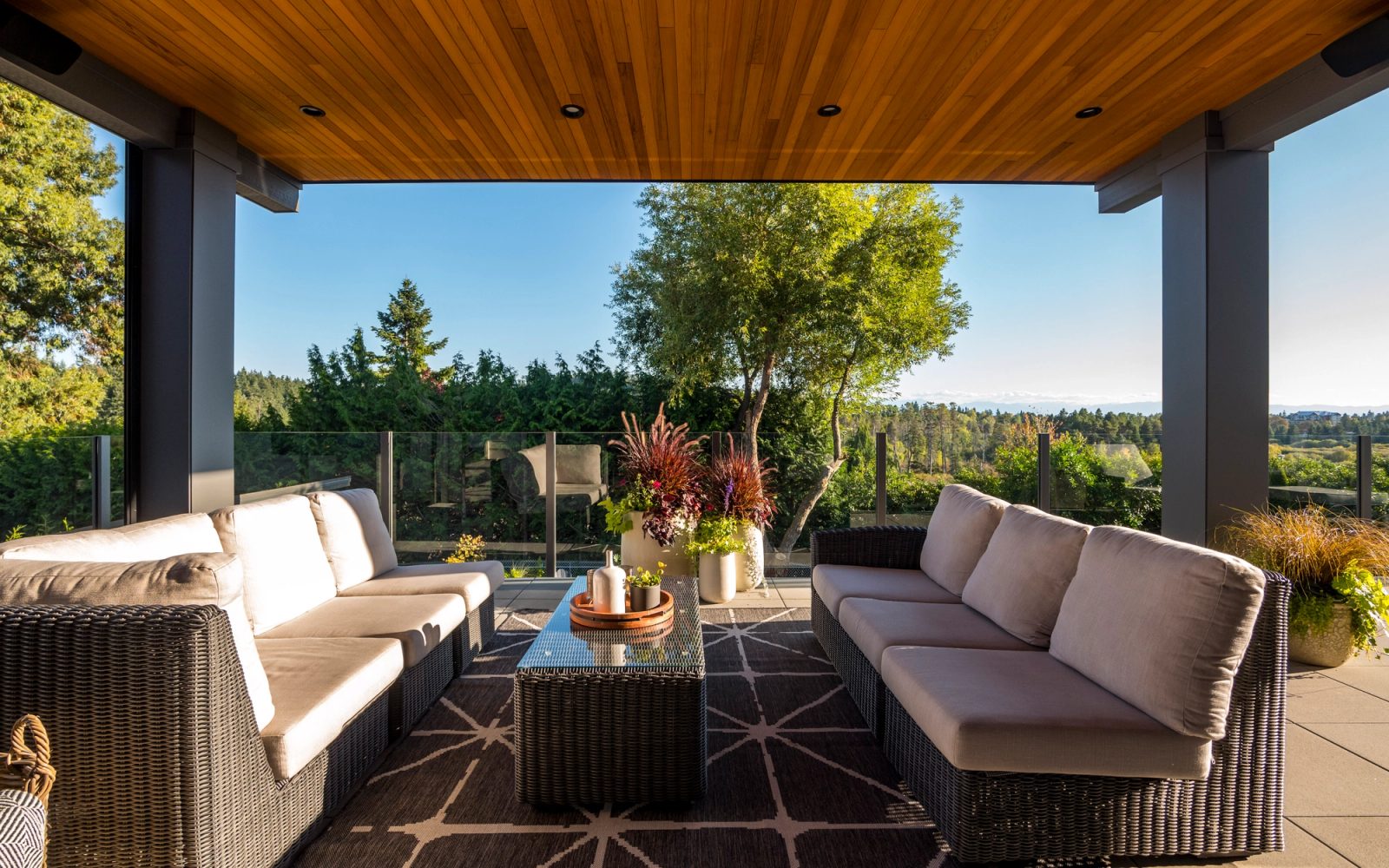 Covered deck with wicker seating under a cedar soffit, looking out over treetops to distant hills