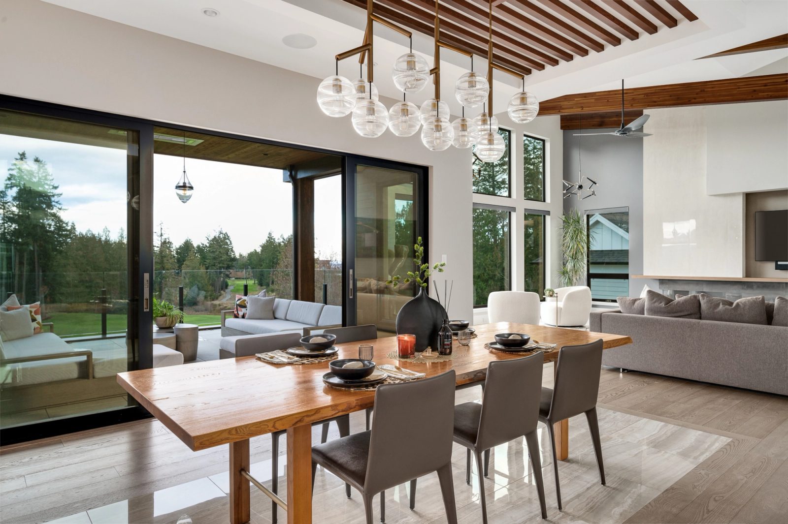 Dining table under twelve blown-glass globes, with sliding doors open to a covered terrace and lawn beyond