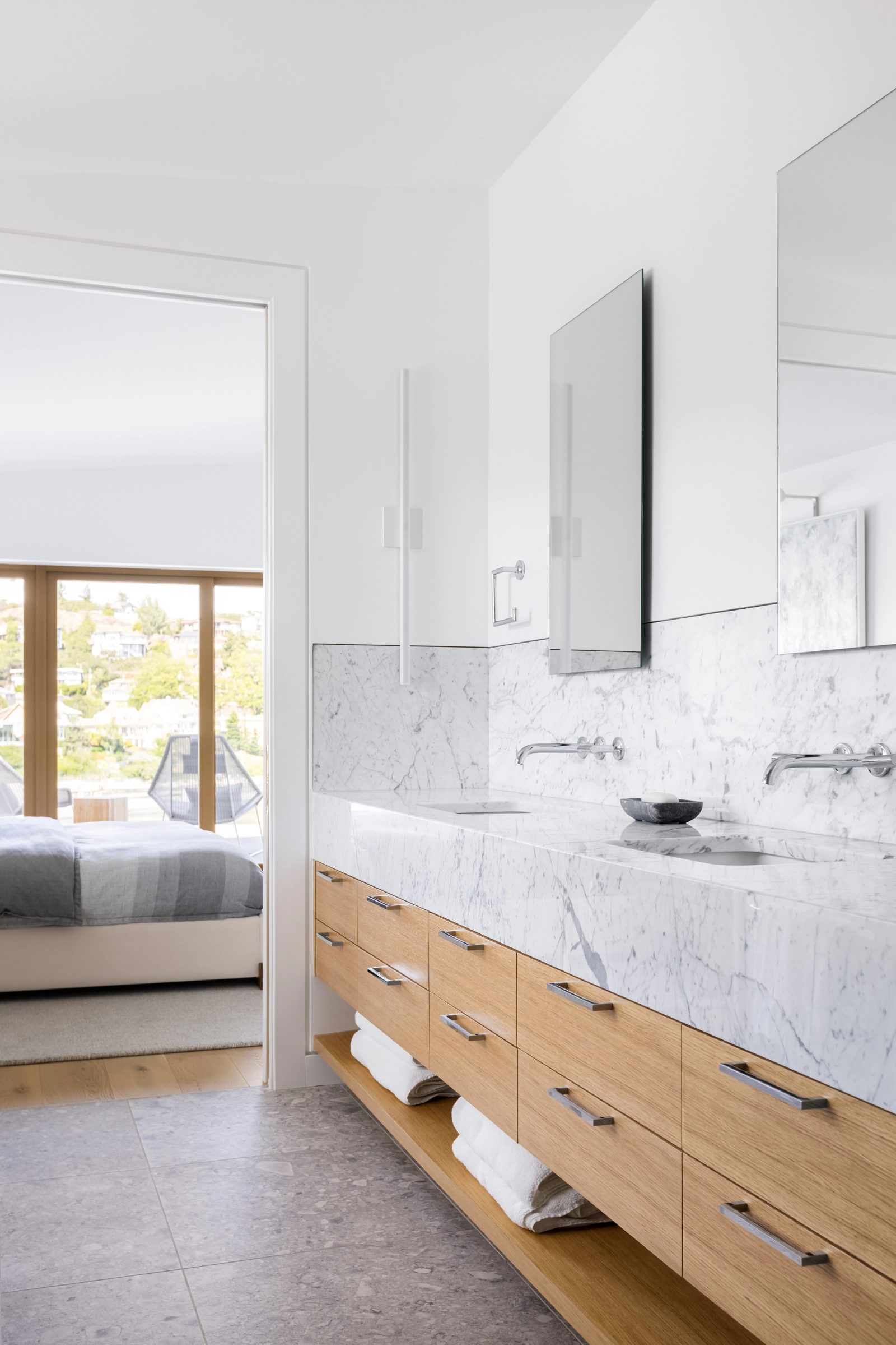 Double marble vanity with wall-mounted taps, folded towels on an open oak shelf below.