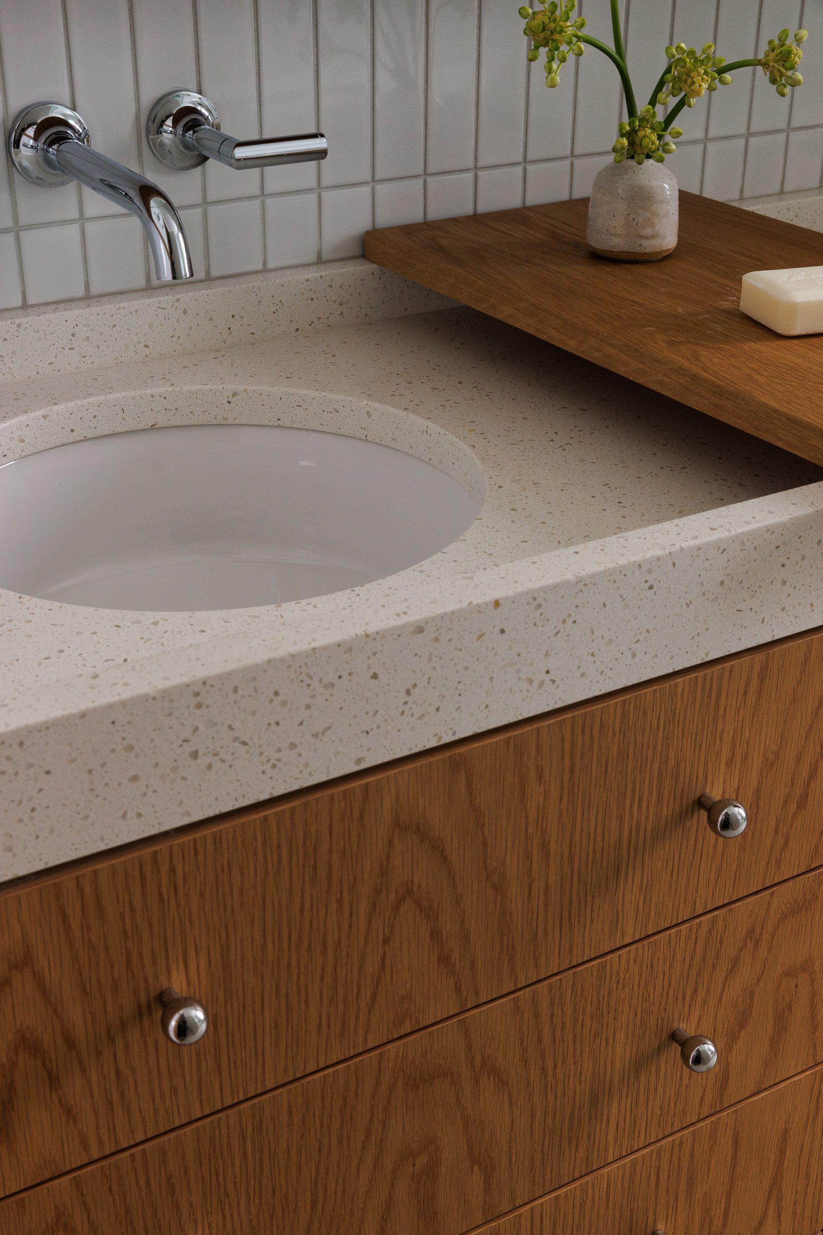 Right: the basin close, a chrome wall spout and an oak tray across the terrazzo.