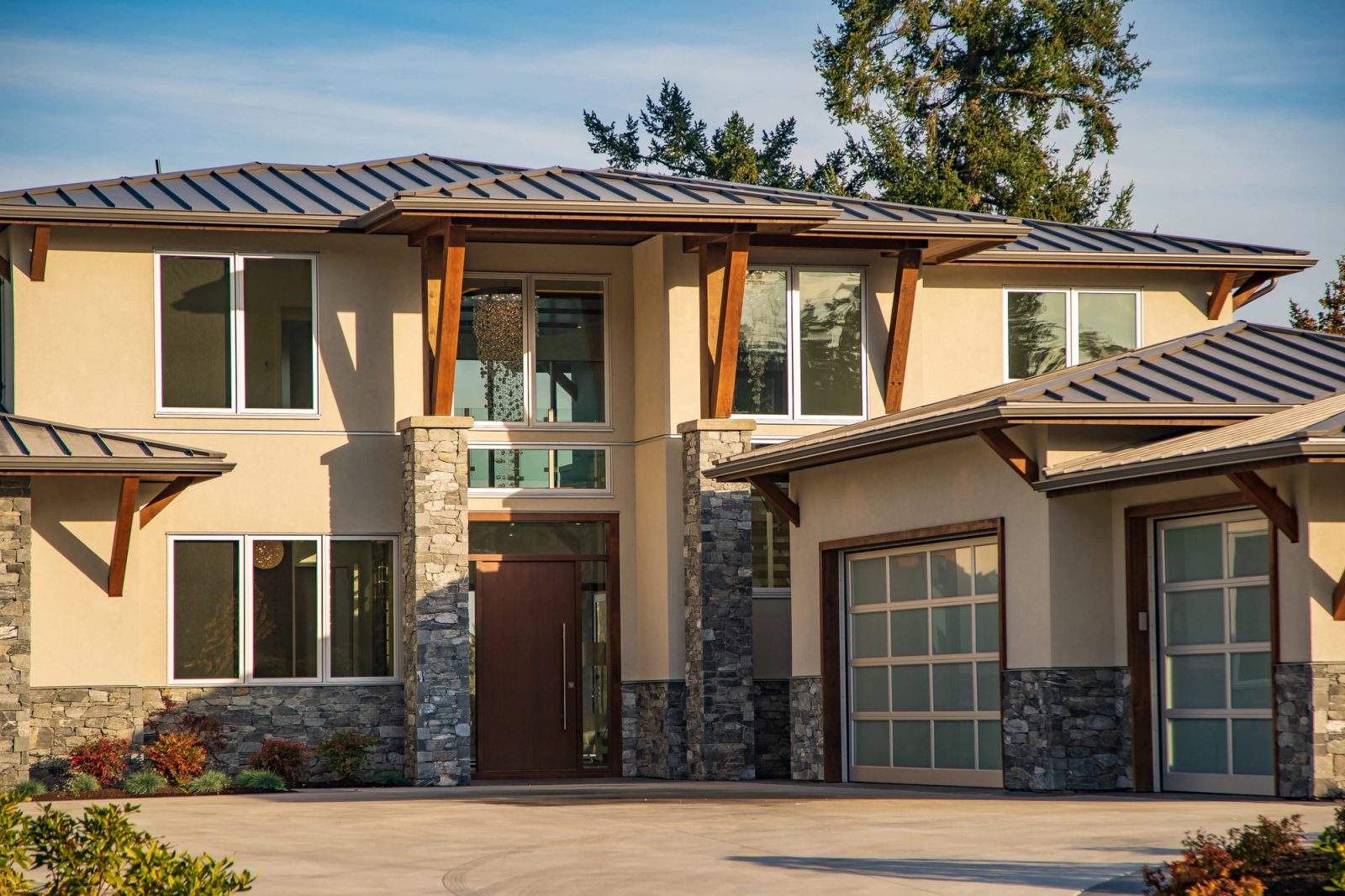 Entry of a stucco and stone house with timber outriggers, a walnut front door and a beaded glass fixture hanging behind full-height glazing