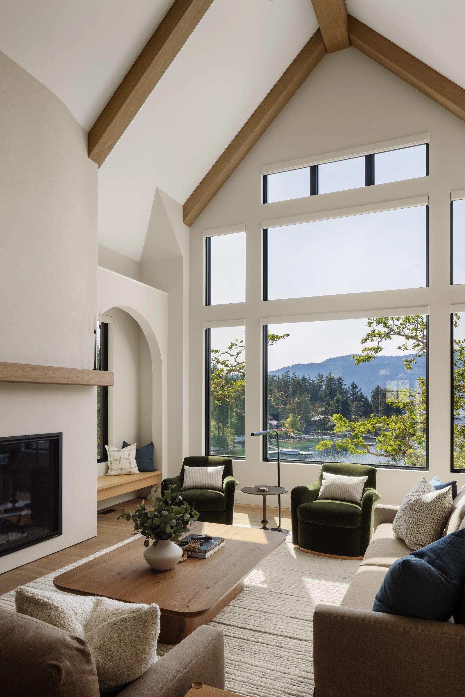 Left: the same room from the hearth, oak beams rising to the ridge and a wall of glass over the cove, green velvet chairs drawn up to it.