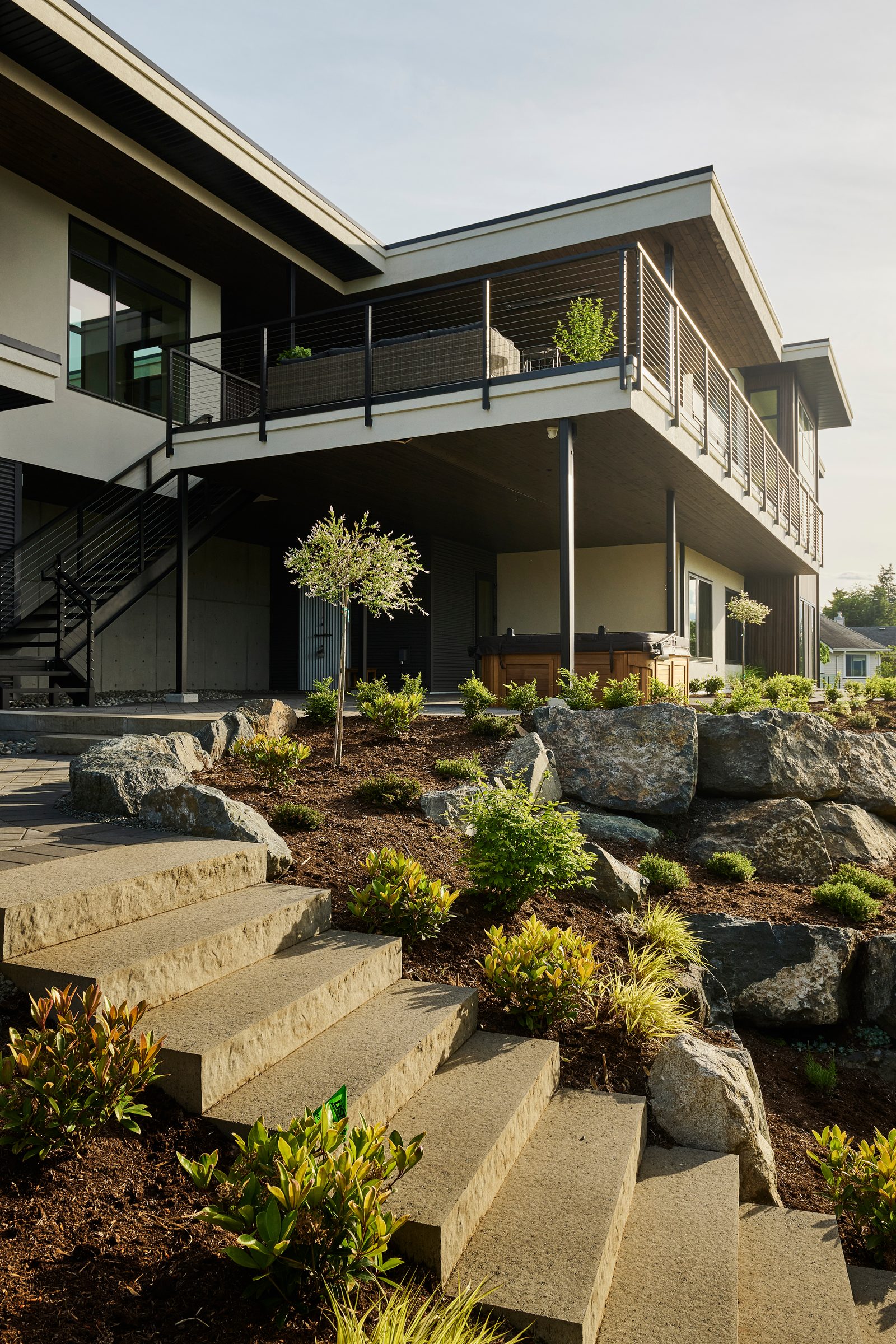 Rear elevation with cantilevered deck, stone steps climbing the planted slope