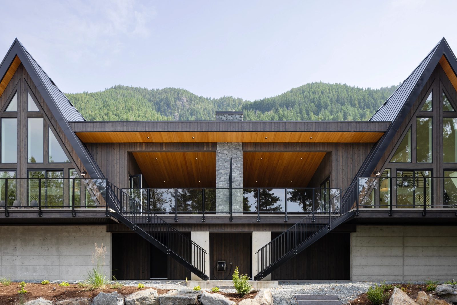 Lake elevation of paired A-frames flanking a covered outdoor room with a stone chimney