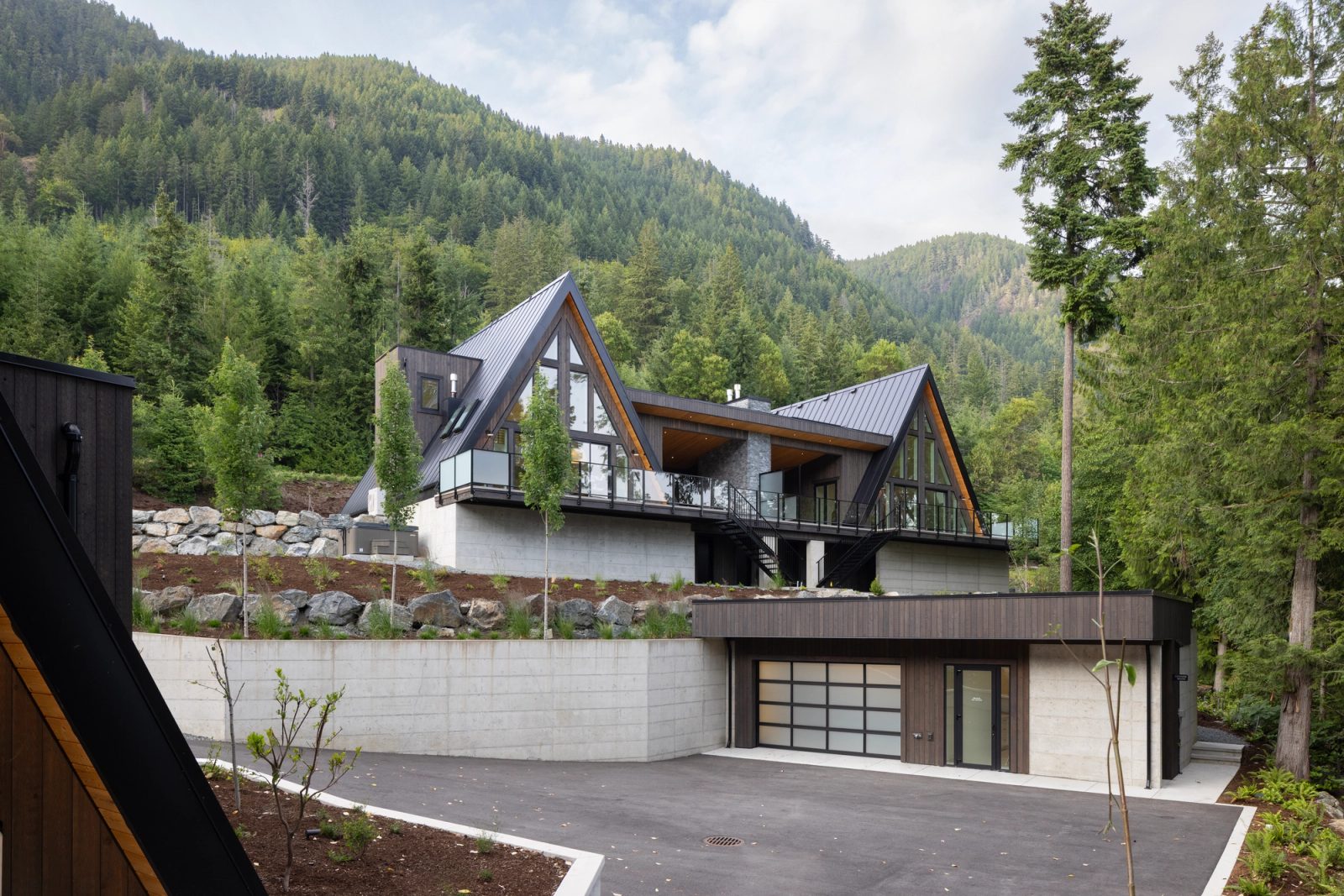 A-frame building on a board-formed concrete podium above a sunk garage, forested slope behind