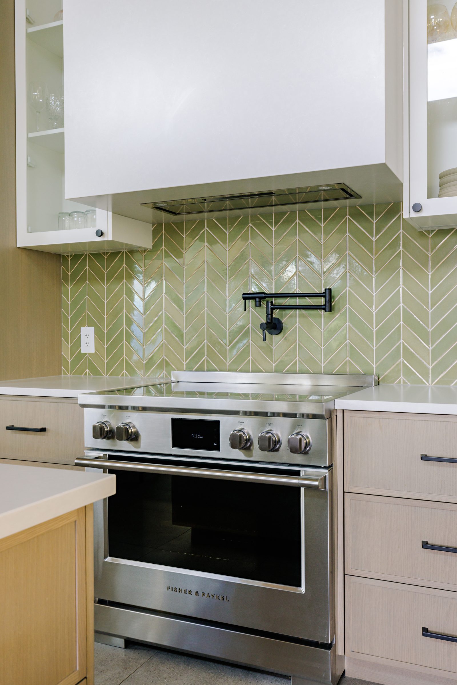 a stainless range set into a green chevron tile backsplash with a black pot filler folded against the wall.