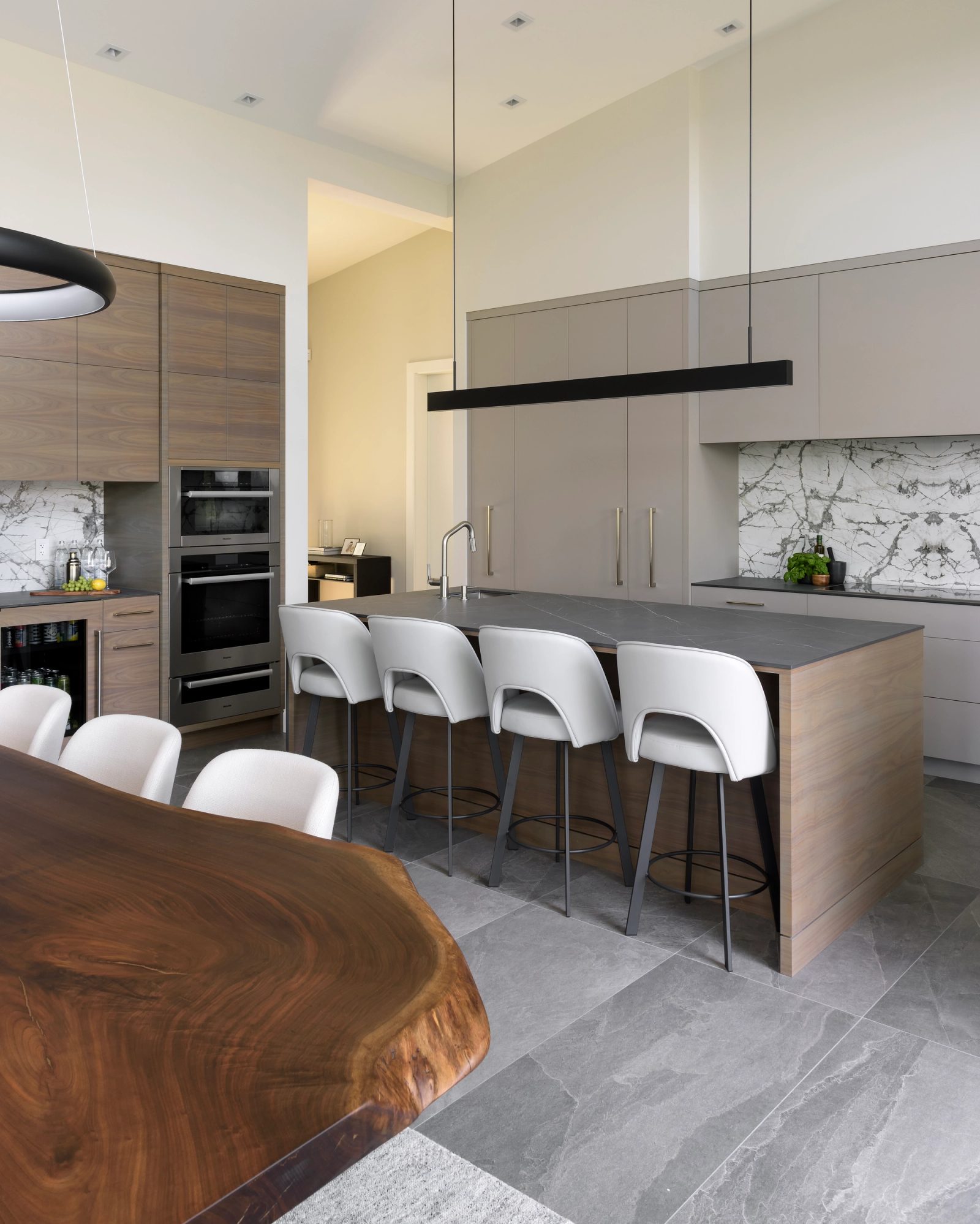 Kitchen island in dark stone with walnut cabinetry, integrated wine storage and a book-matched marble backsplash