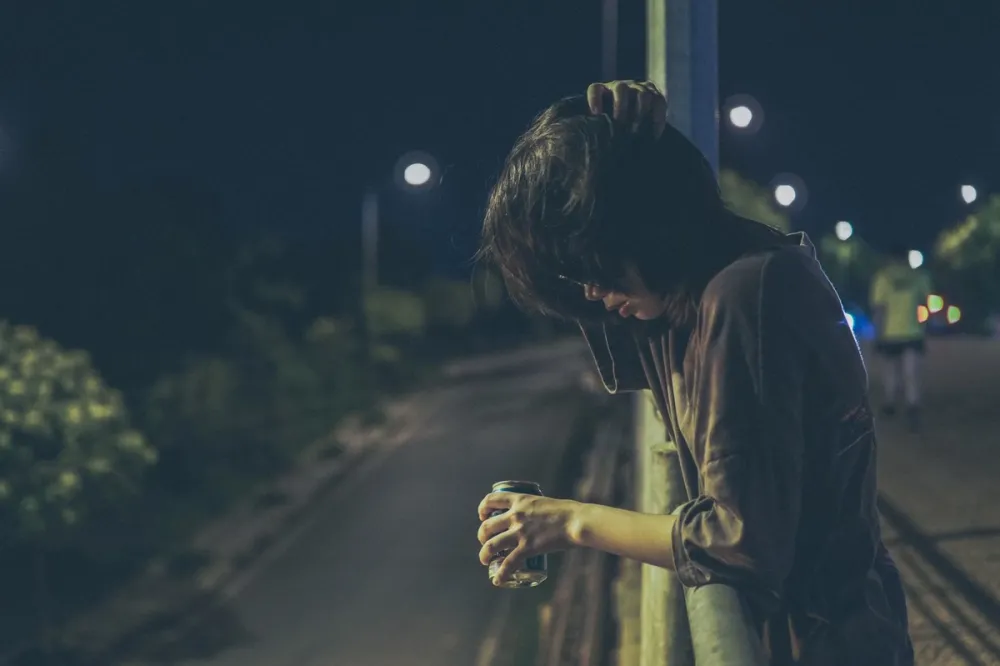 밤거리 난간에 기대 캔 음료를 들고 고개를 숙인 사람