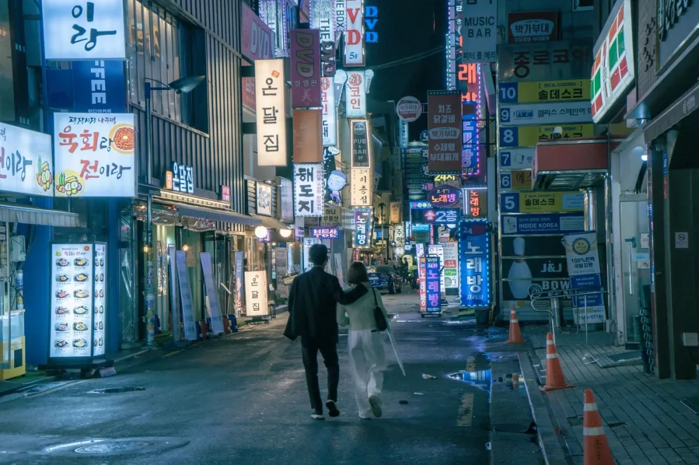 간판 불이 켜진 밤 골목을 나란히 걸어가는 남녀의 뒷모습