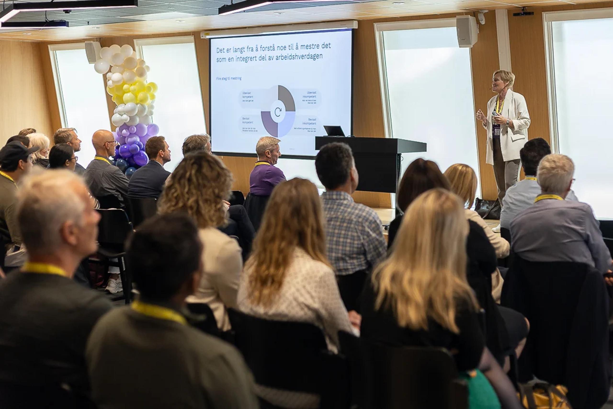 Bilde av publikum som lytter til person som holder innlegg om viktigheten av endringsledelse