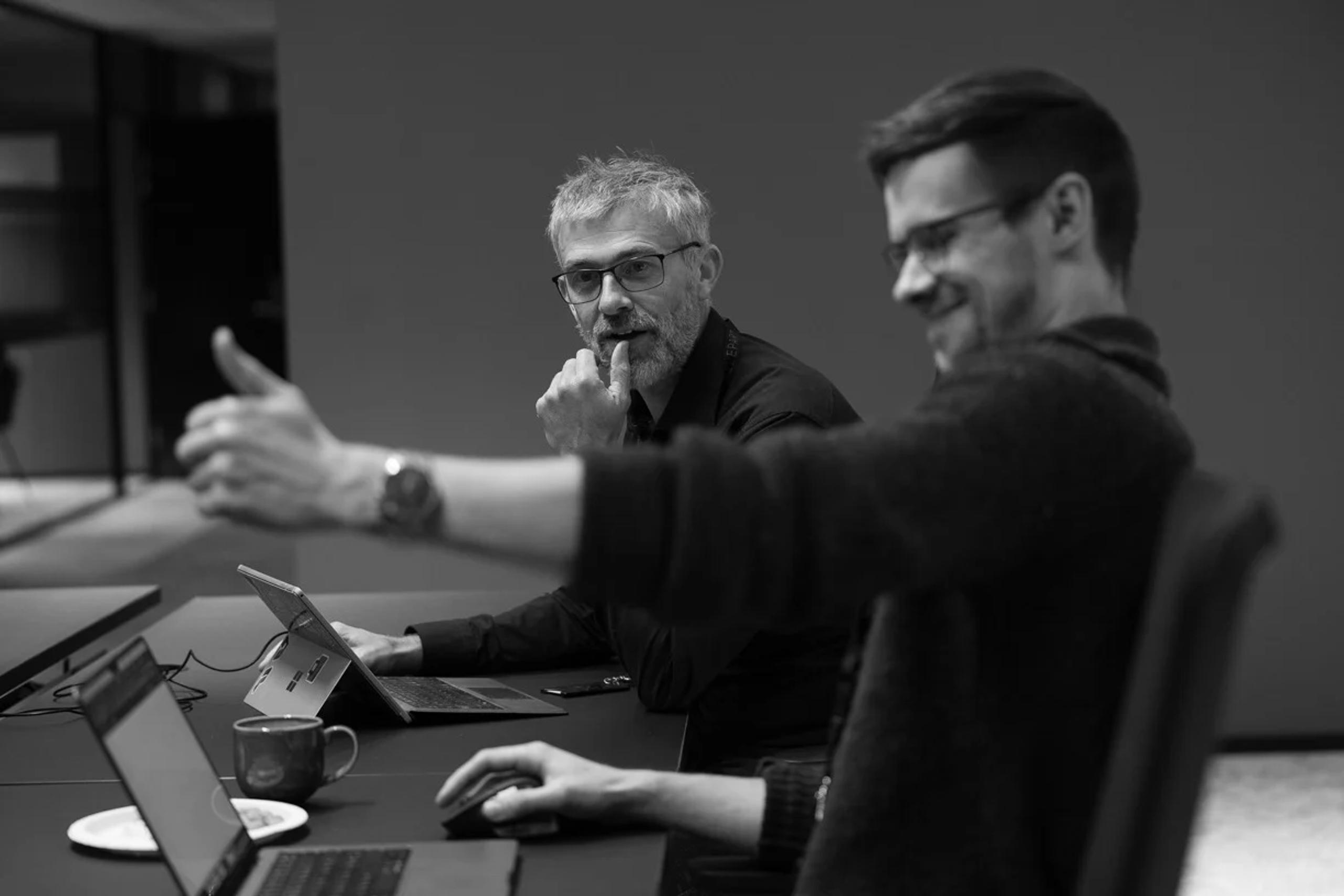 Bilde av kollegaer som snakker sammen forran PC-skjerm