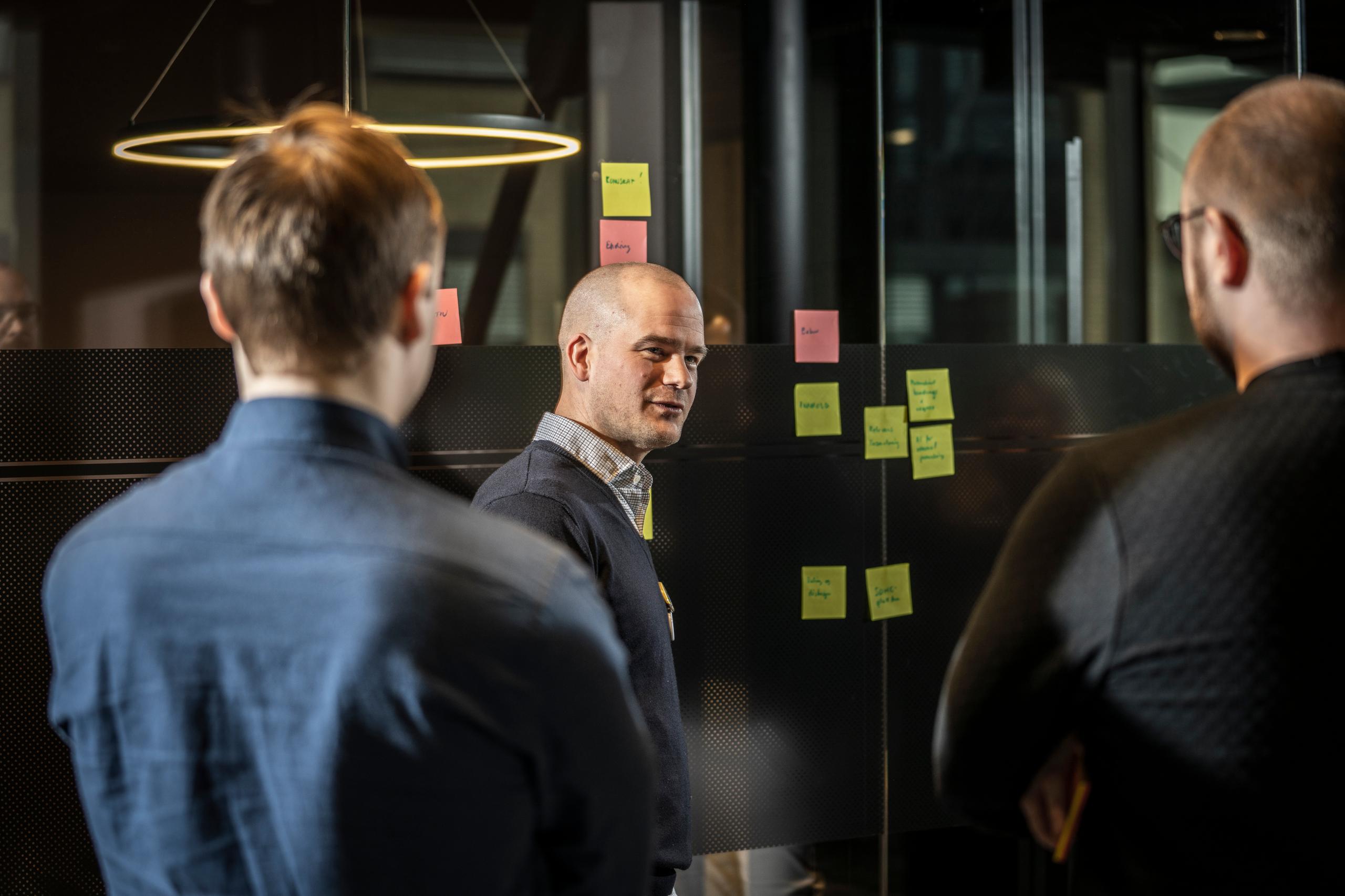 Inmetaer diskuterer utfordring foran vegg med post-it lapper