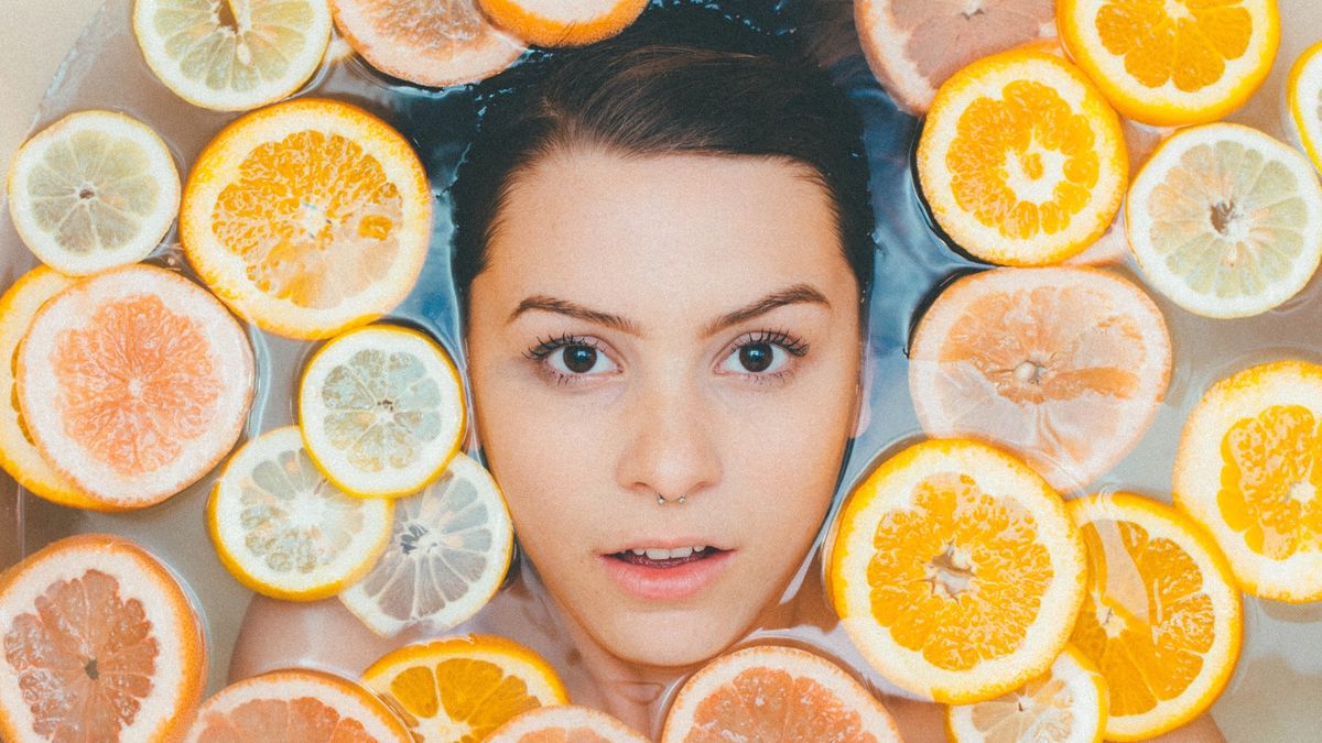 Girl with clear skin in water surrounded by orange slices