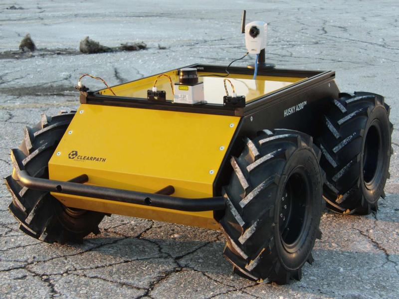 Photo of Husky shows a compact yellow base with sensors and other equipment, and four large tough tires.
