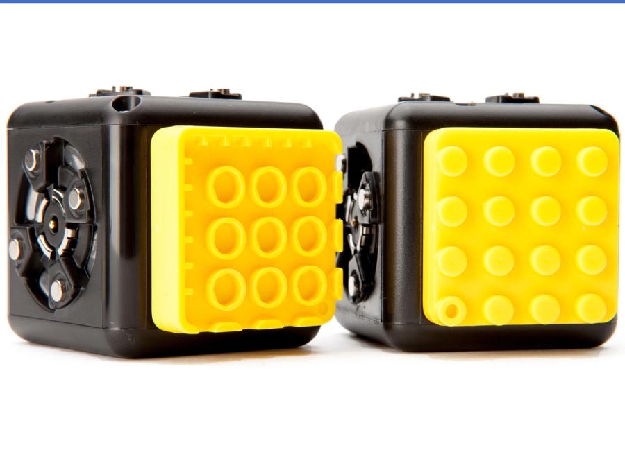 Two robotic cubes with a yellow piece attached to connect to Lego.