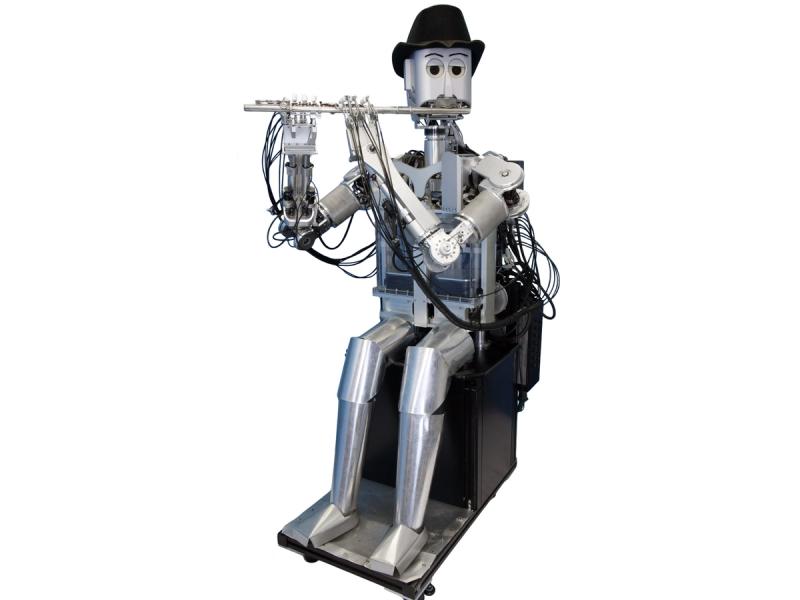 A seated silver humanoid robot whose torso and arms highlight many black wires wears a black hat and plays a flute against a white background.