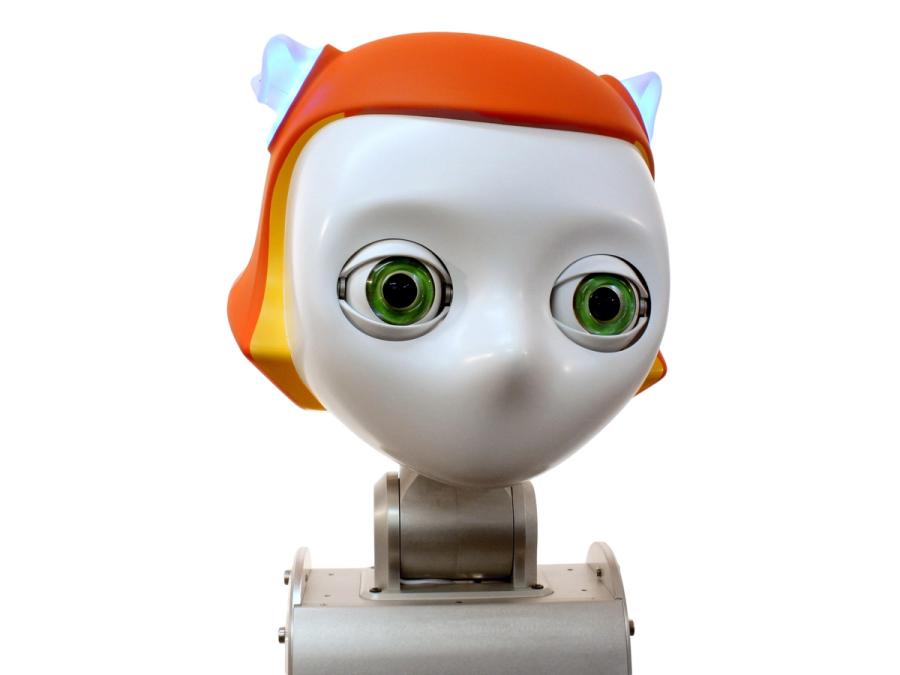 Close up of a robots head. The robot has an orange headpiece, glowing blue cat ears and large green eyes.