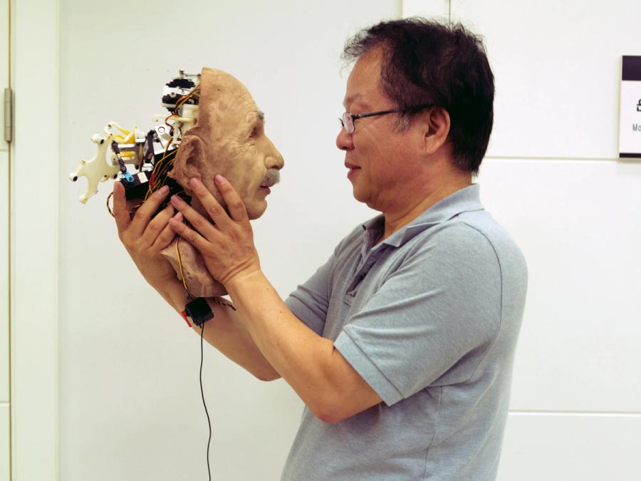A man holds the face of a robot up to his face.