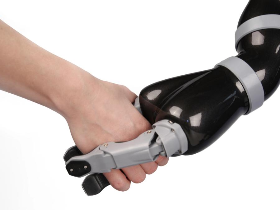 A shiny black and silver three-fingered robotic arm shakes hands with a human.