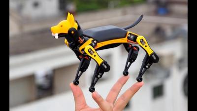 Small robot dog made of black and yellow plastic stands on a person's hand.