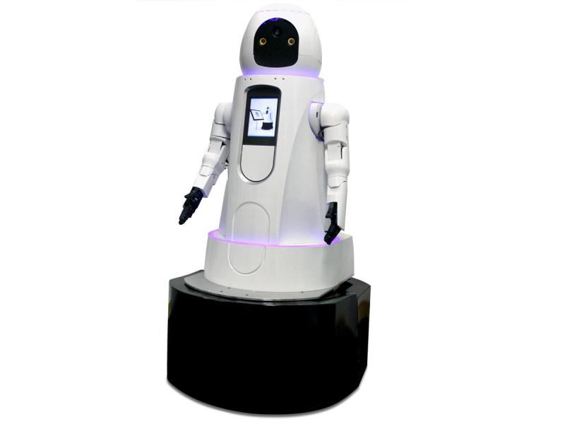 A white cylindrical robot which is wider at its black base has a display screen on its torso, two hands with five black fingers each, and a simple black and white face. A ring of purple light at its neck and the bottom of it's torso are glowing.