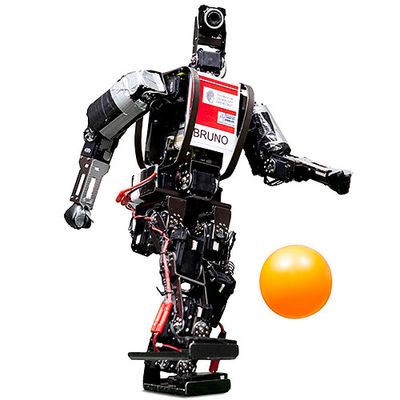 A black two-legged robot labelled Bruno kicks a orange ball.