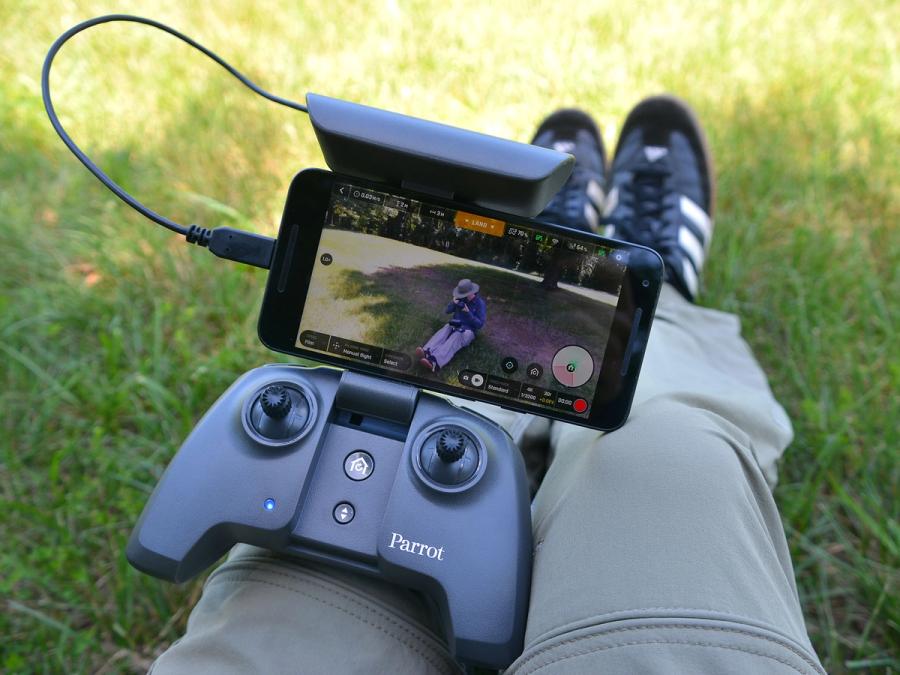 A controller for the drone and a phone showing the drone's view sit on a persons lap.