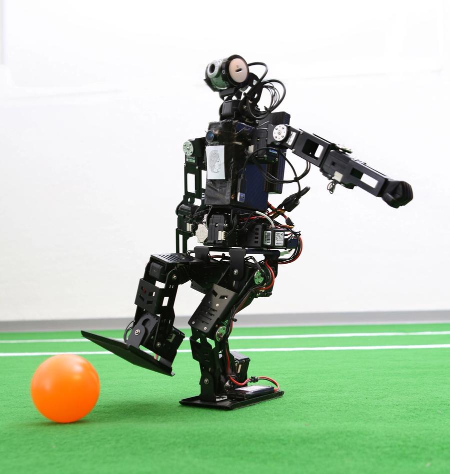 A black robot kicks an orange ball.