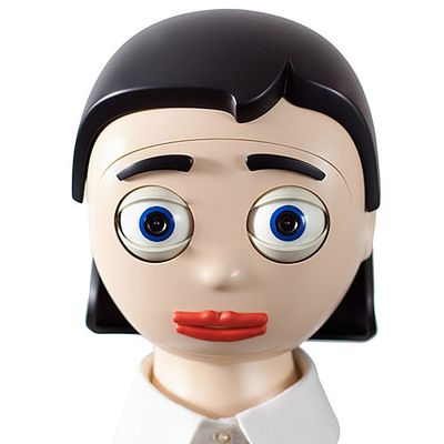 A cartoonish robotic head with big blue eyes with cameras, red lips, and black eyebrows and a black, bobbed hairdo sits on a base.