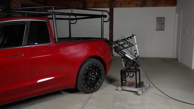 A four-wheel robotic device with an articulated arm inserts a car charger into a red EV truck in a garage.