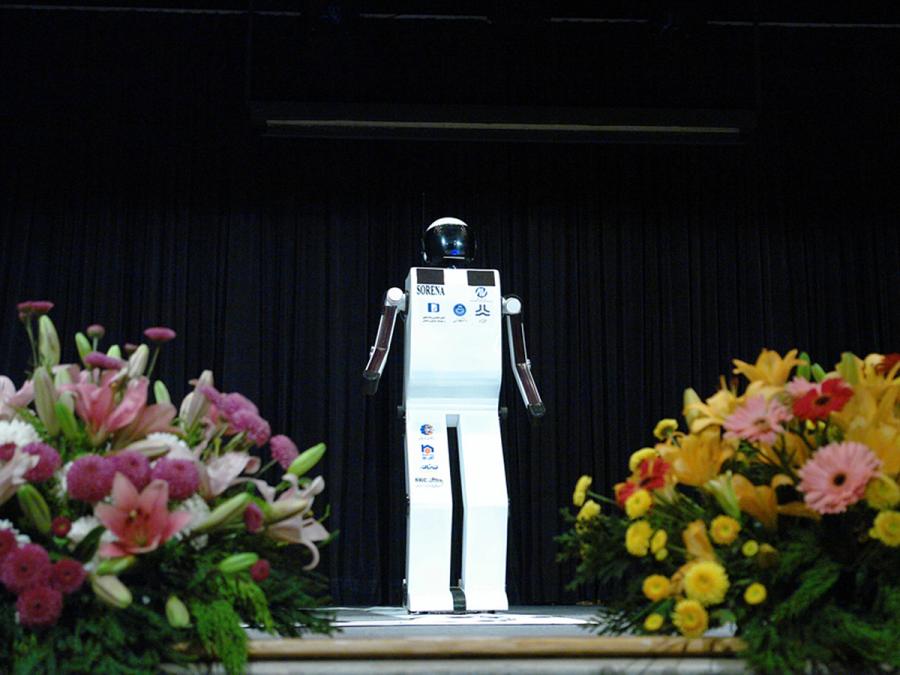 The first Surena humanoid robot presented on a stage in front of flowers.