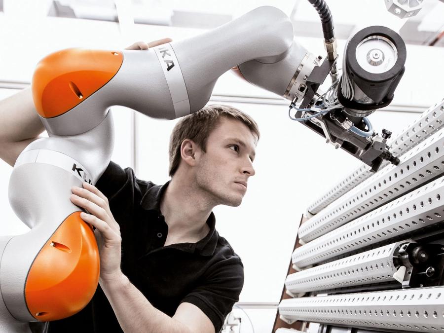 A man holds the robot arm in place as its arm attachment reaches towards a white object.