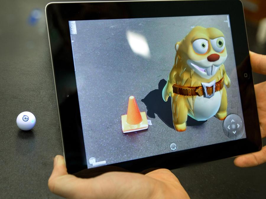 Hands hold an iPad which show a cartoonish yellow beaver standing up next to an orange construction cone.