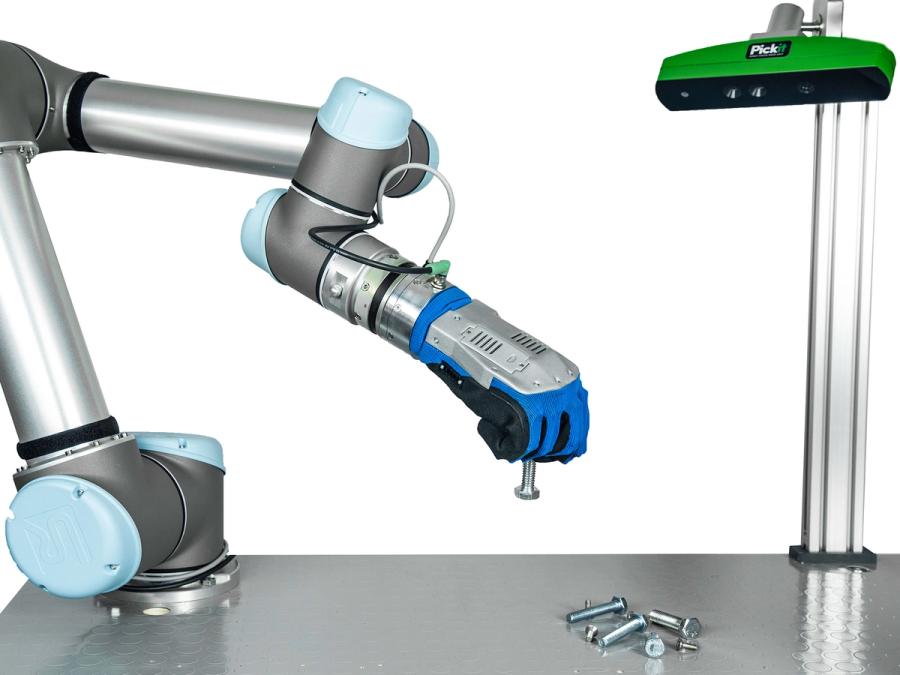 A robotic hand attached to a Cobot arm on a tabletop pinches a bolt between two fingers. The hand has metal on top, and is covered in blue and black soft material. On the right side of the table, a pole holds a camera system looking at the hand.