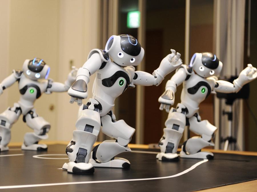 Three white and silver humanoid robots doing coordinated dance moves.